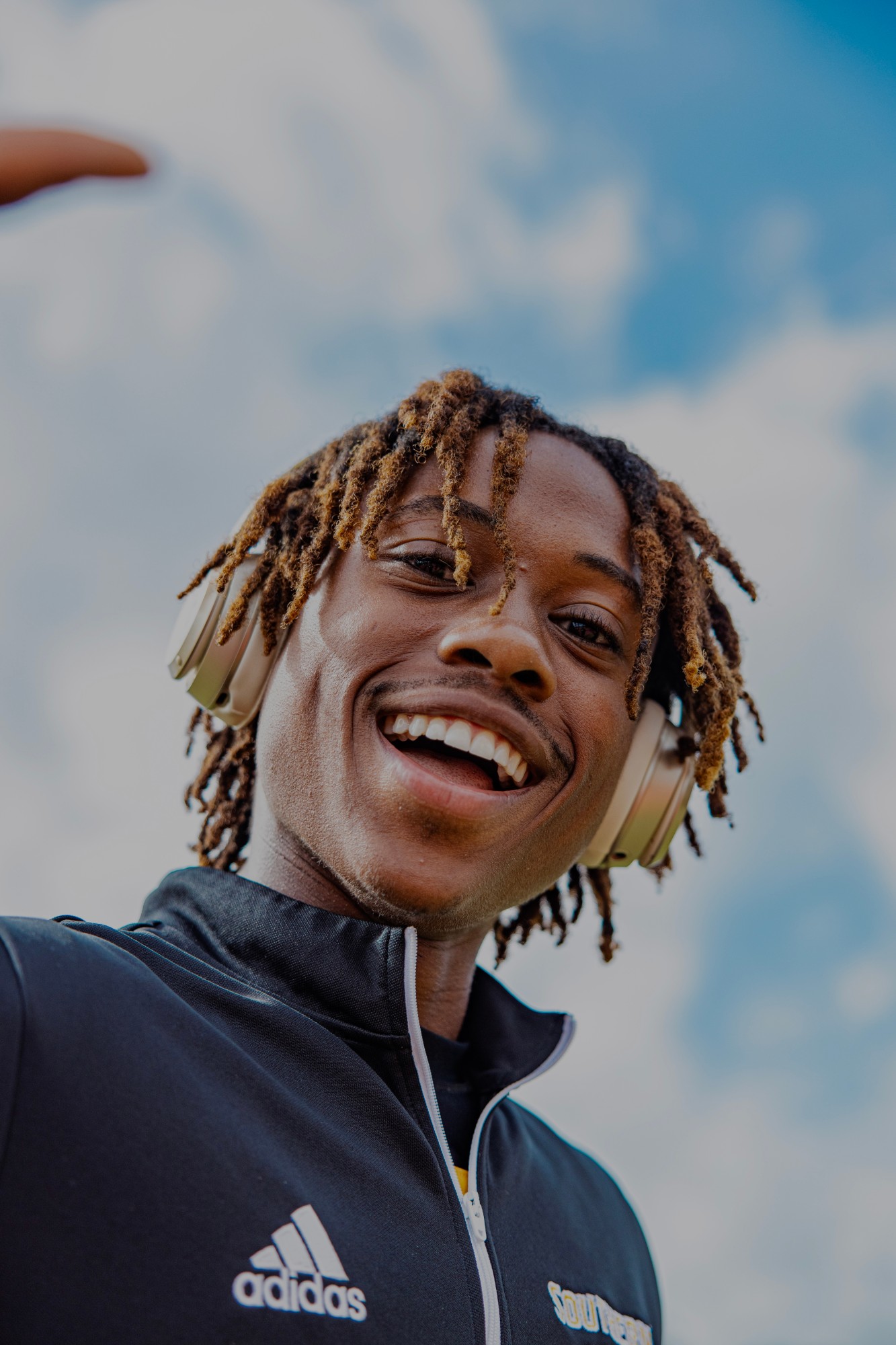 Tyler Nichols smiling in a Southern Miss warm-up jacket and headphones under a blue sky